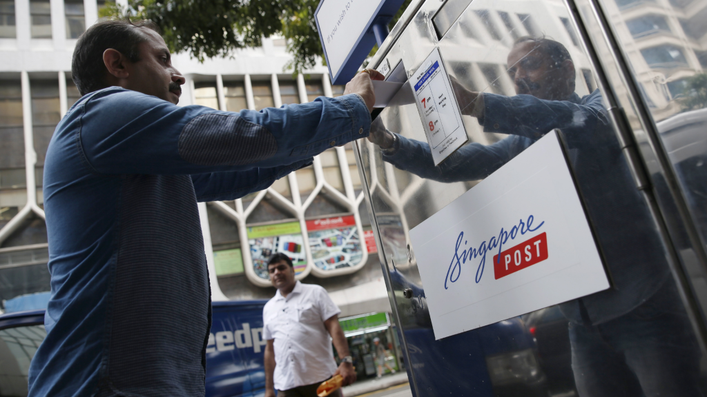 A man drops a letter into a SingPost mailbox. (Photo: Reuters)