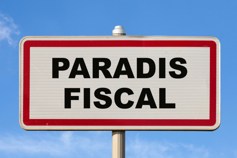 A French entry city sign against a blue sky with written in the middle in French "Paradis fiscal", meaning in English "Tax haven".